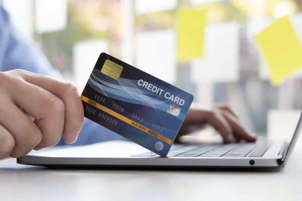 Hand holding a credit card while making an online payment on a laptop