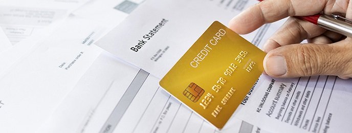 A hand holding a gold credit card over bank statements and documents, symbolizing a pre-approved credit card offer.
