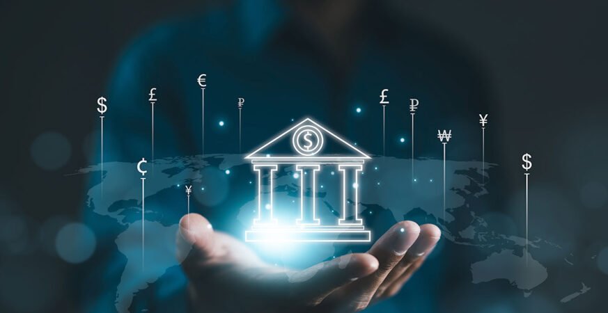 Hand holding a glowing digital icon of a central bank building surrounded by various global currency symbols over a world map background.
