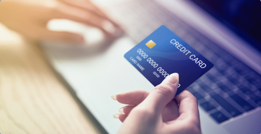 A person holding a blue credit card in front of a laptop during an online payment process